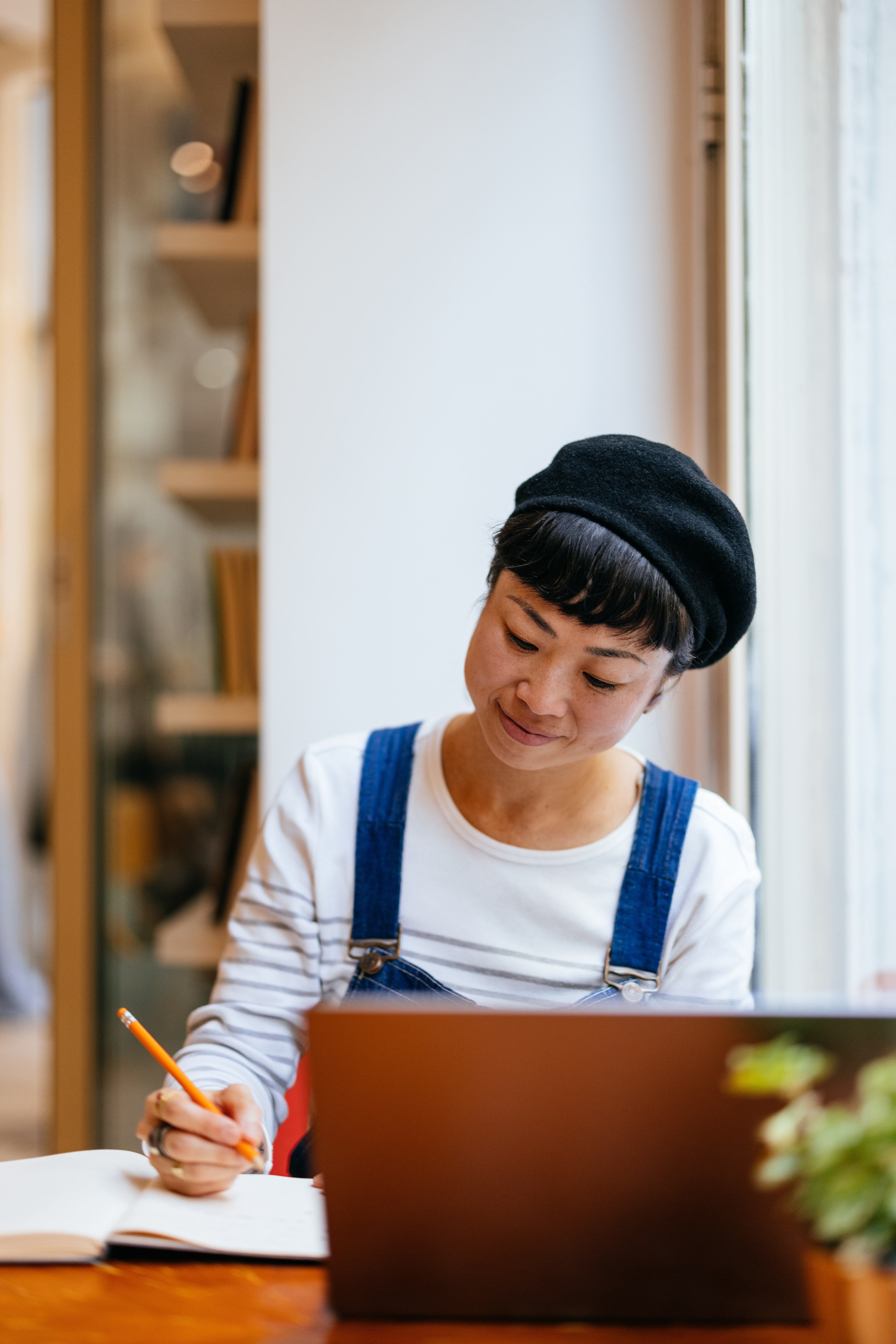 Woman Making Notes Using Laptop At Cafe