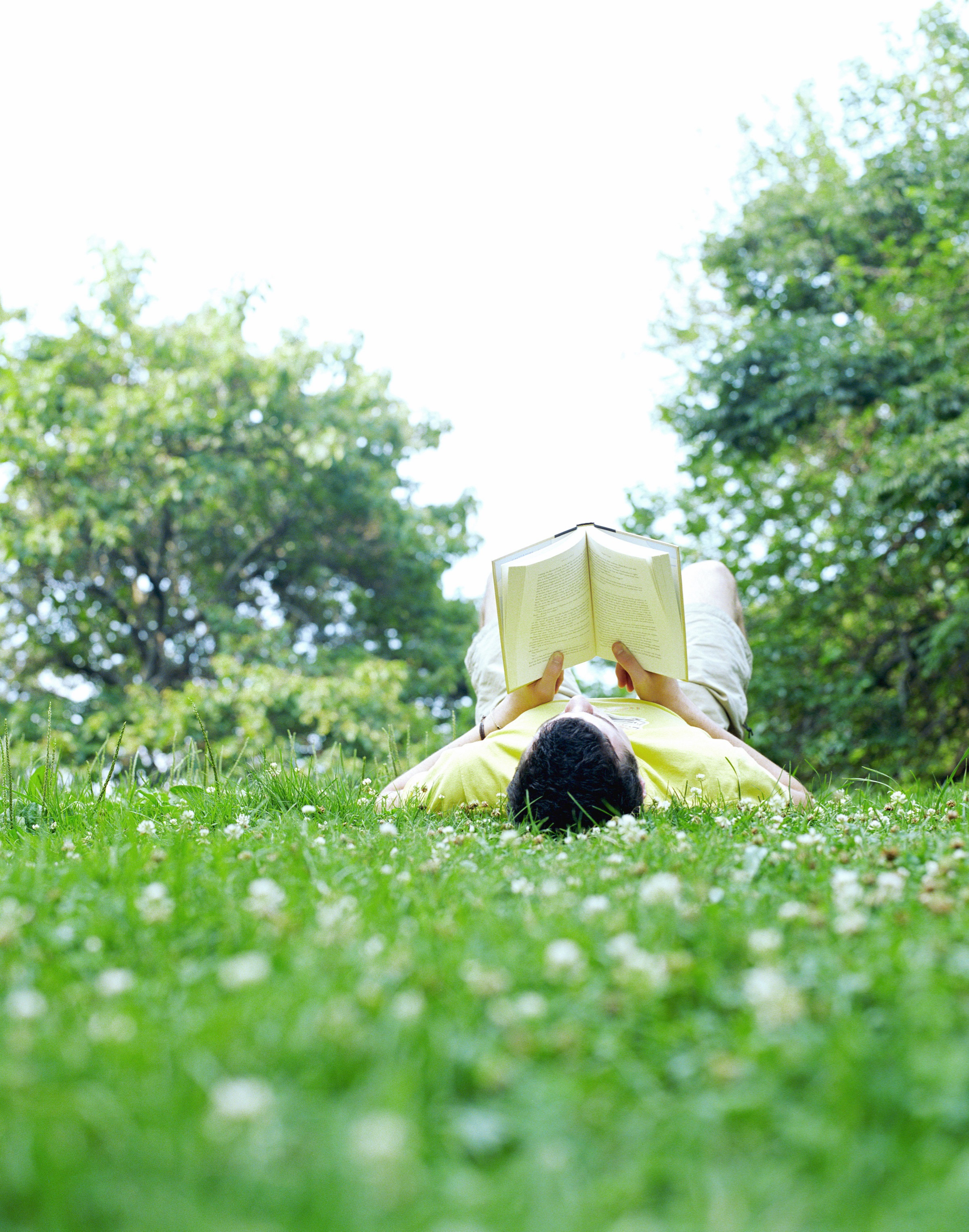 Man Reading a Book Laying in a Grassy Field Outdoors