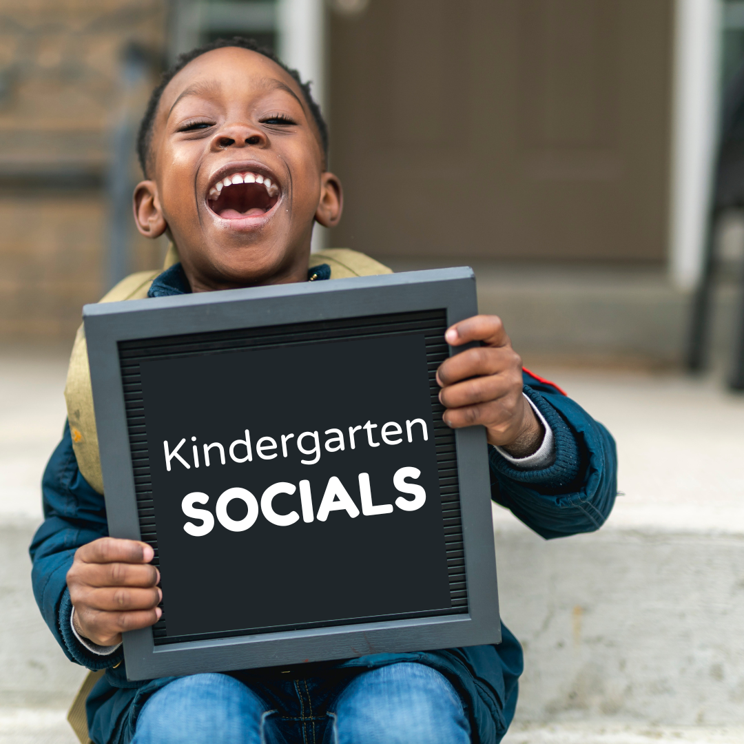 A young boy with a wide smile holds a letter board which reads "Kindergarten socials".