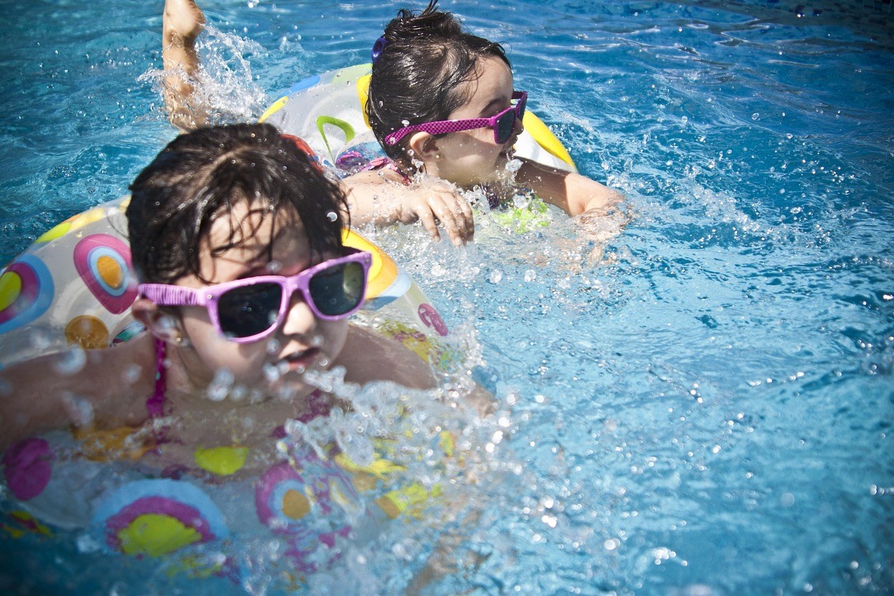 A photo of two young girls swimming in sunglasses and inflatable innertubes. 