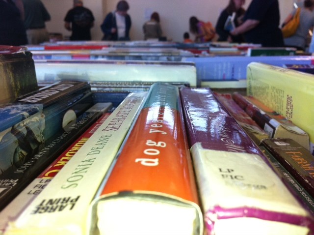 A photo of books and shoppers at a library used book sale.