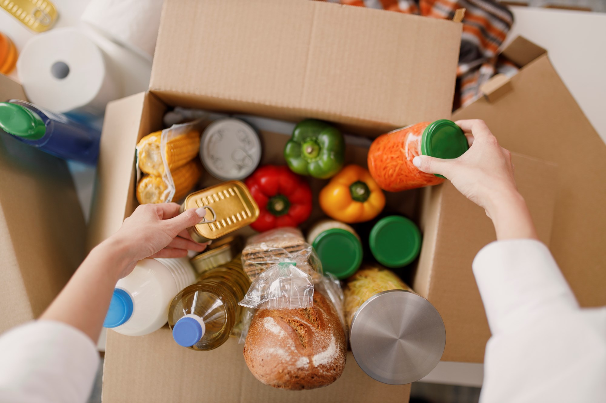 A unseen person fills a cardboard box with food.