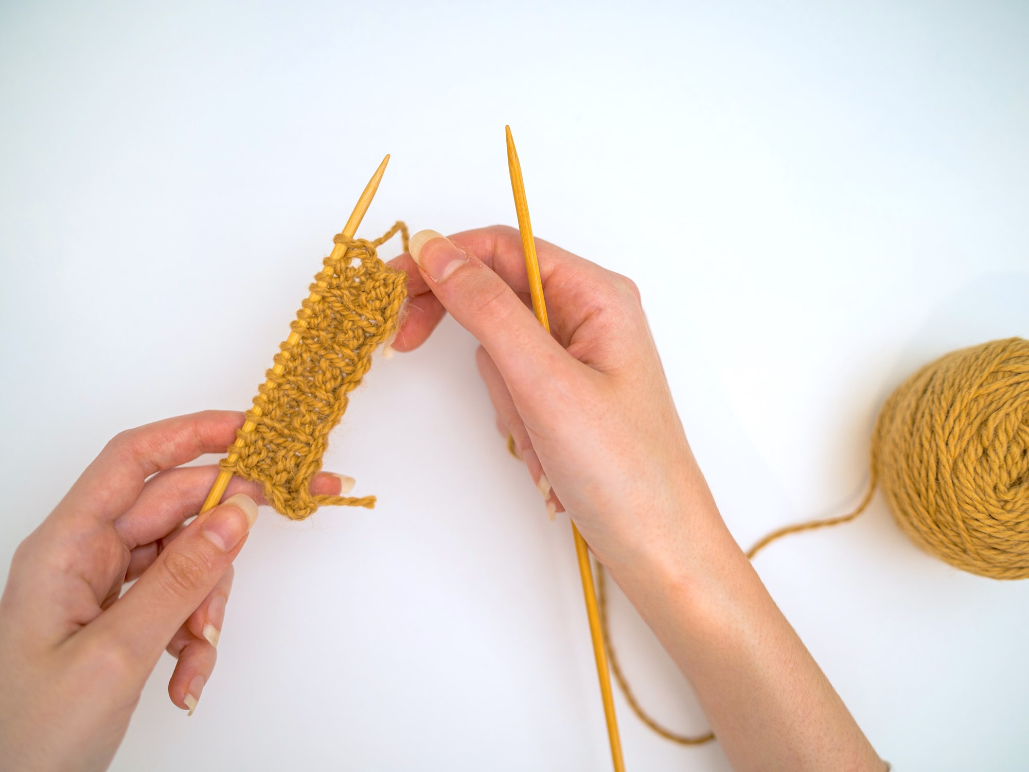 A photo of someone knitting with yellow yarn.
