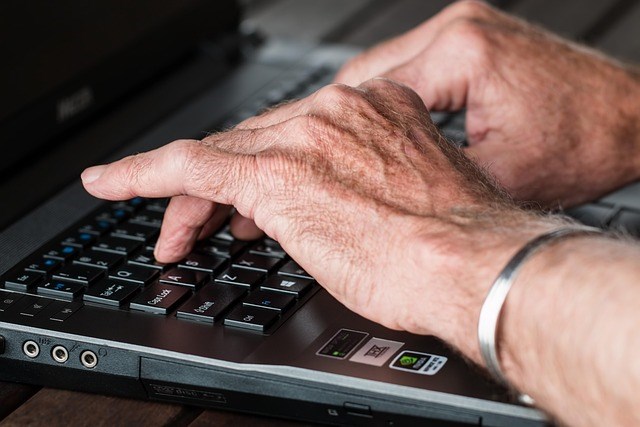 A photo of an older adult typing on a laptop.