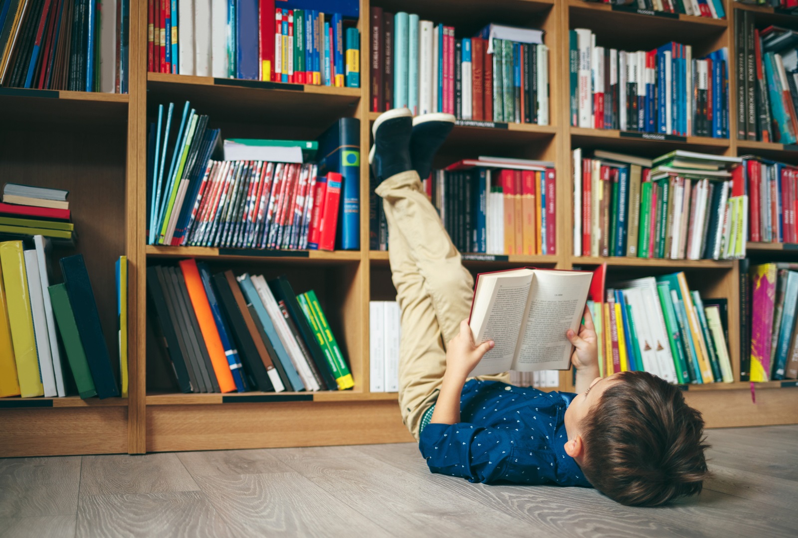 Boy laying on ground reading with feet resting on a shelf