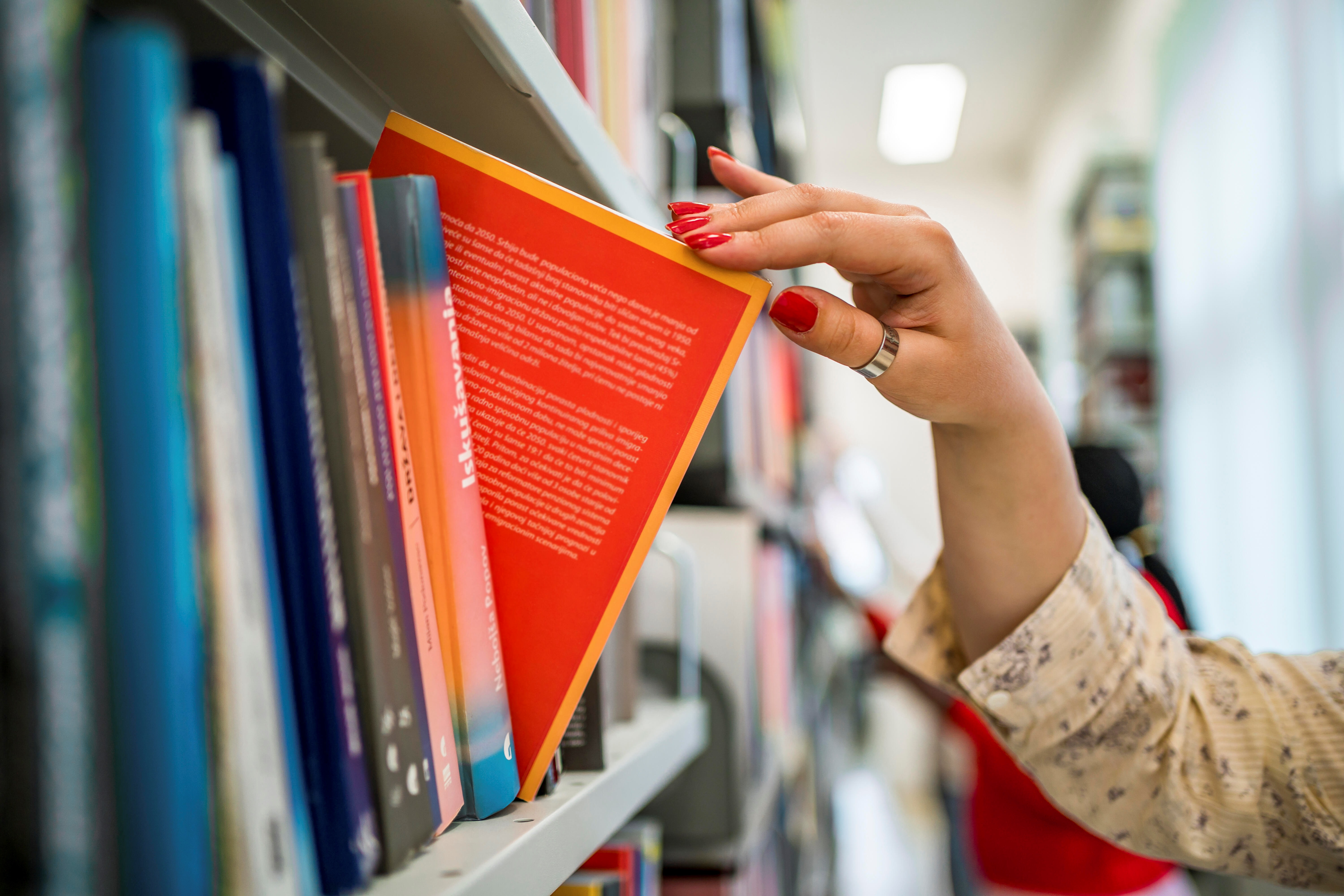 Woman Hand Picking a Book from a Library Bookshelf