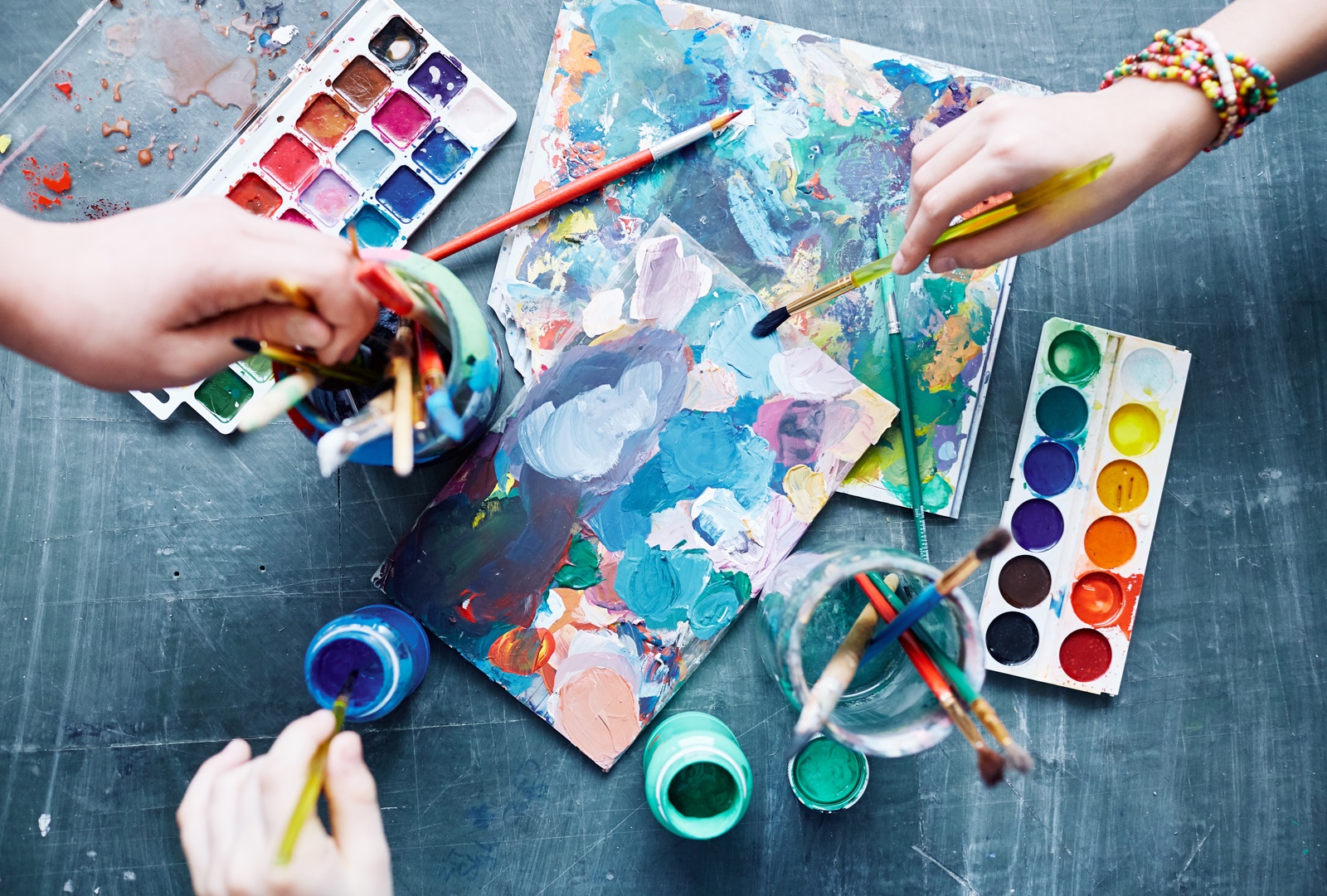 several hands holding paint brushes working on shared canvas
