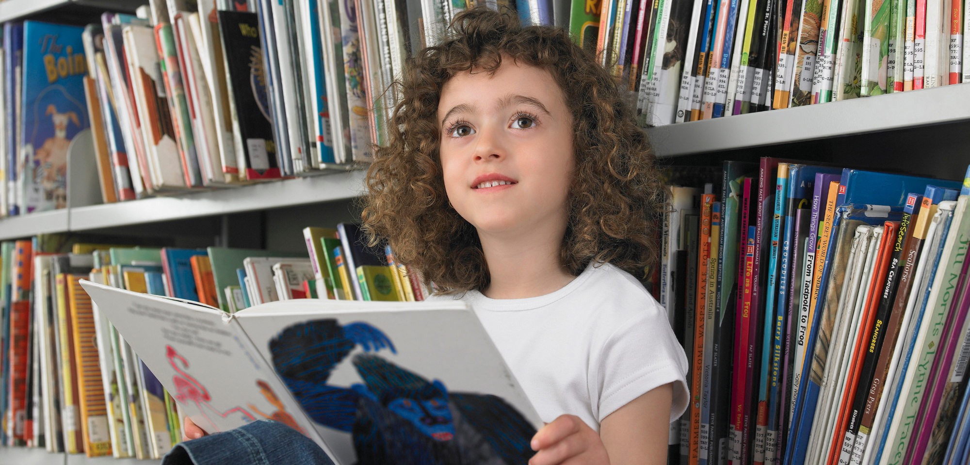 A child sitting with their back to a bookshelf; an Eric Carle picture book open on their lap.