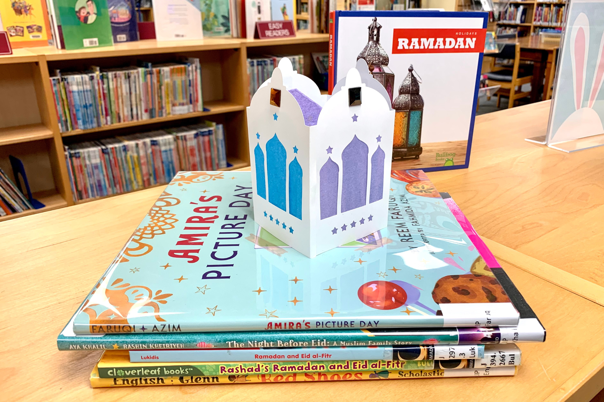 A paper lantern craft rests on top of a small stack of children's Ramadan picture books.