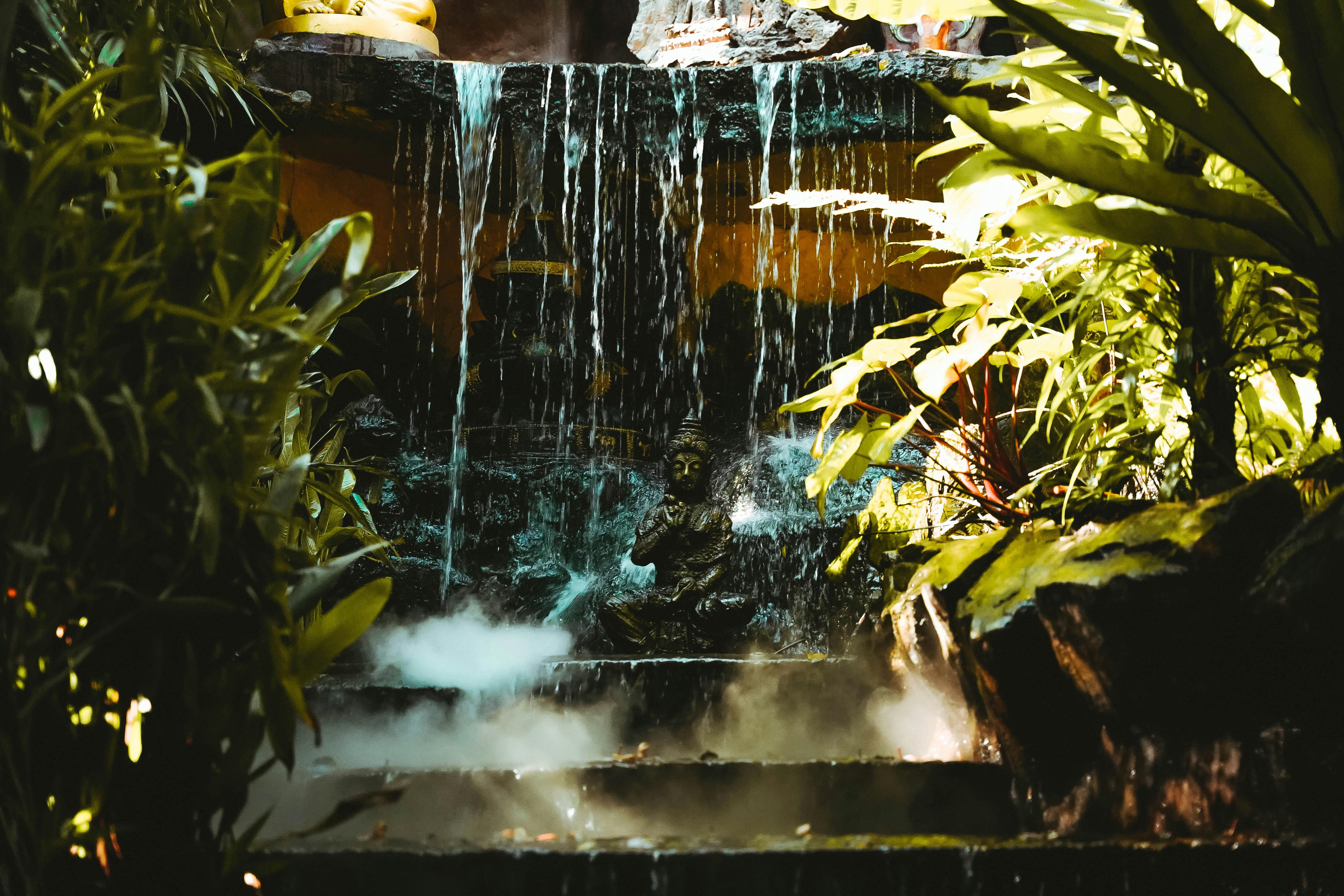 Statue of Buddha under a Waterfall with Lush Foliage