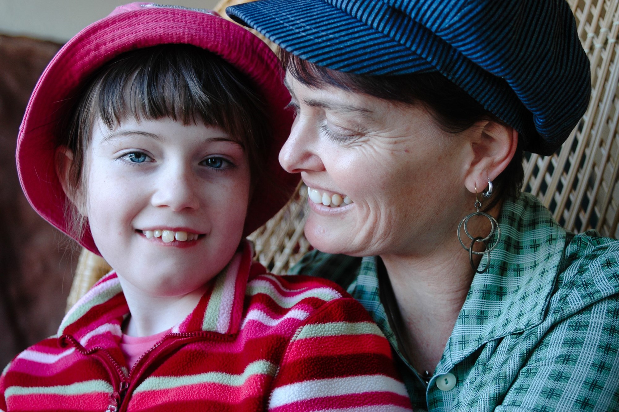 A middle age mother with a school age child on here lap, both wearing hats