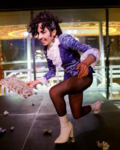 San Sax smiling and lunging in a Prince costume with high-heeled boots