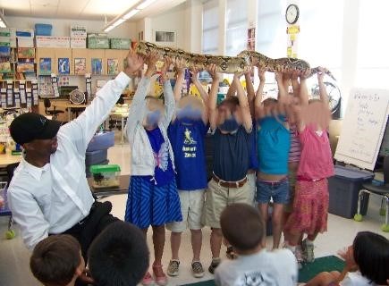Some children are holding a snake besides an instructor, everyone is having fun