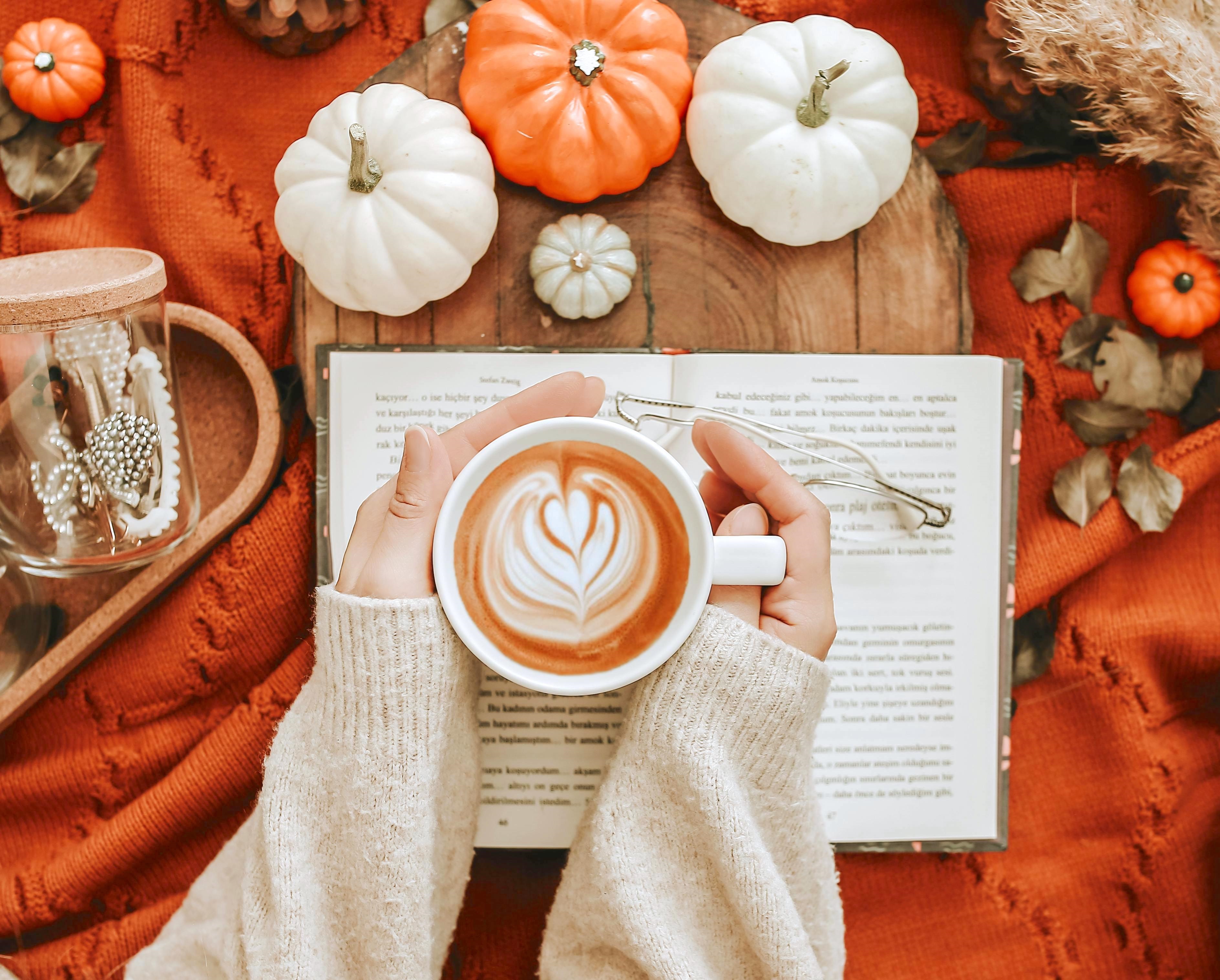 Person Holding a Coffee Mug Over an Open Book in a Fall ScenePumpkins