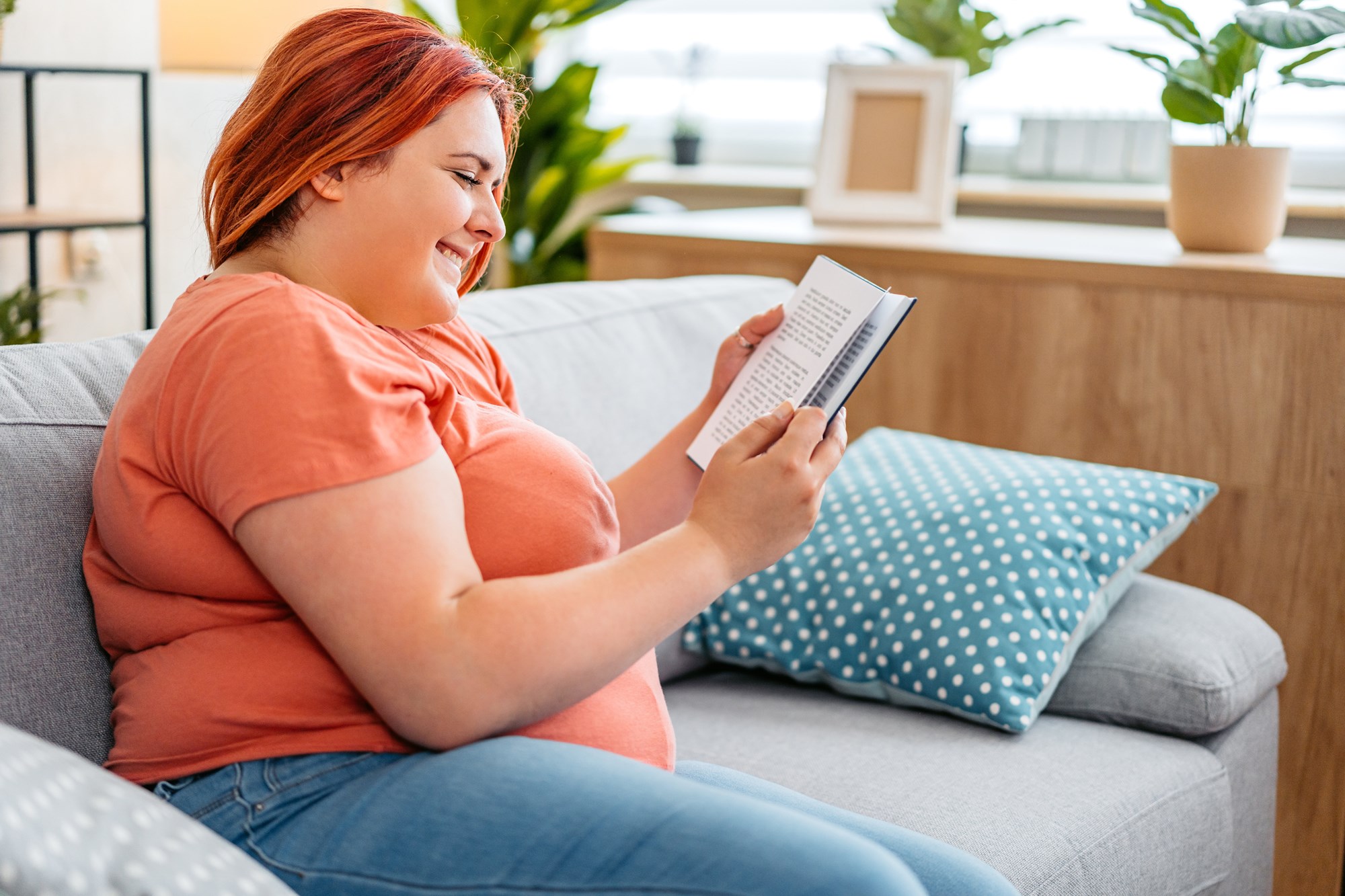 Young Woman Reading A Book While Sitting On The Sofa At Home