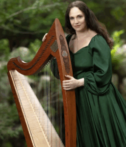 Photo of standing woman in green silk gown with long dark hair holding large wooden Celtic upright harp
