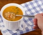 Bean soup in white fluted container on a blue and white cloth being spooned out by a male hand
