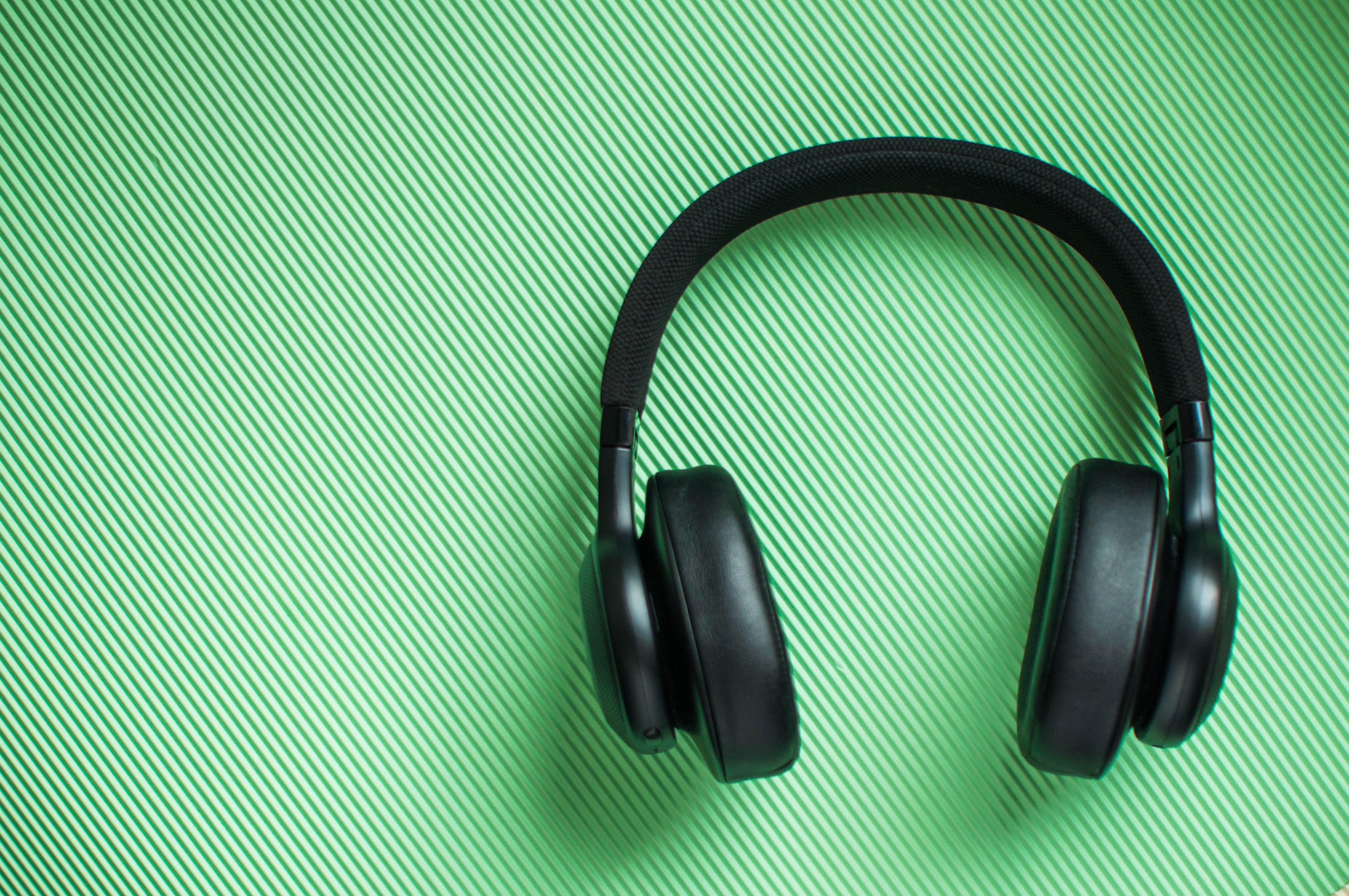A Flat Lay of Black Pair of Headphone on a Green background