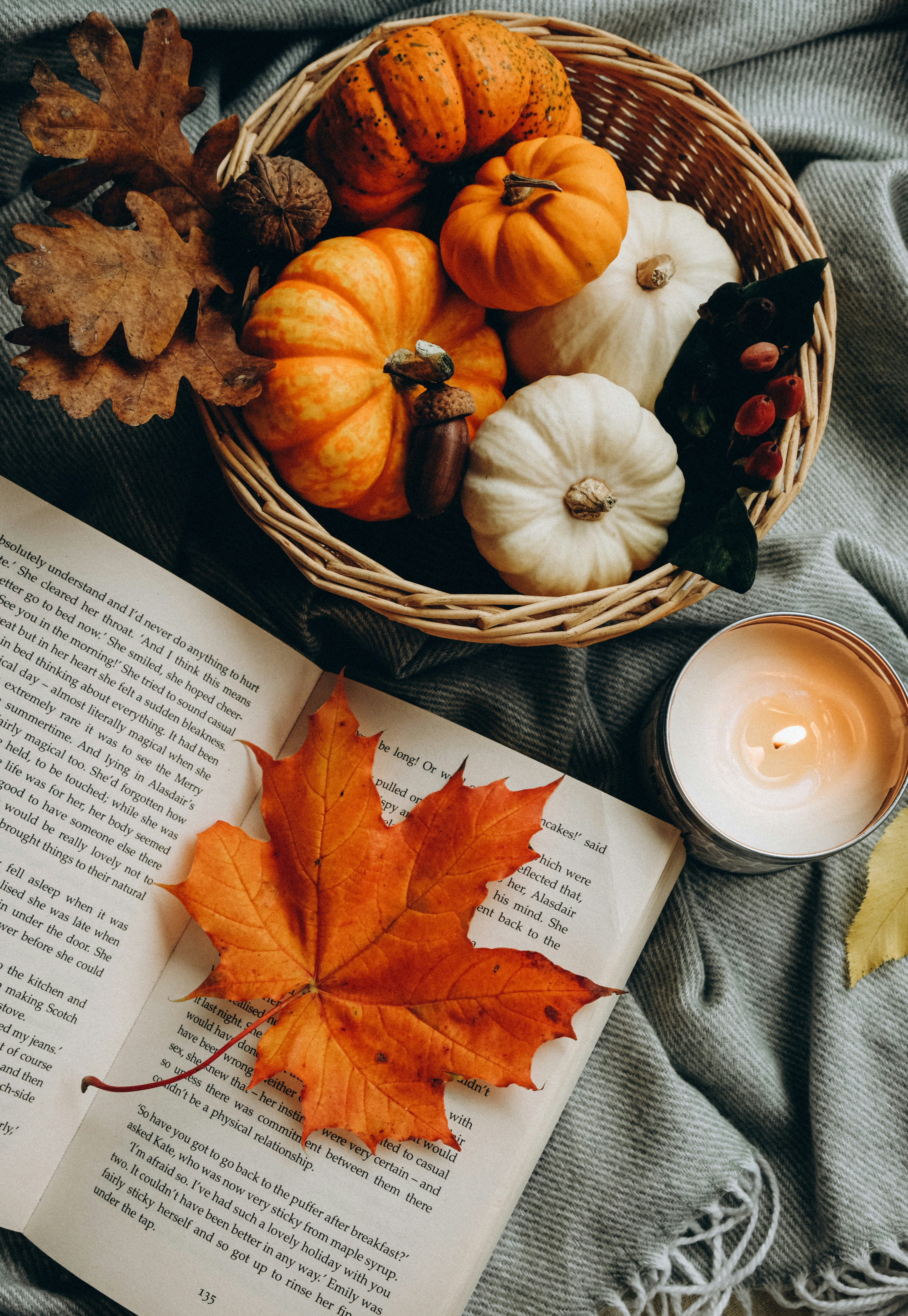 Open Book with an Orange Leaf Next to a Basket of Mini Pumpkins and a Lit Candle