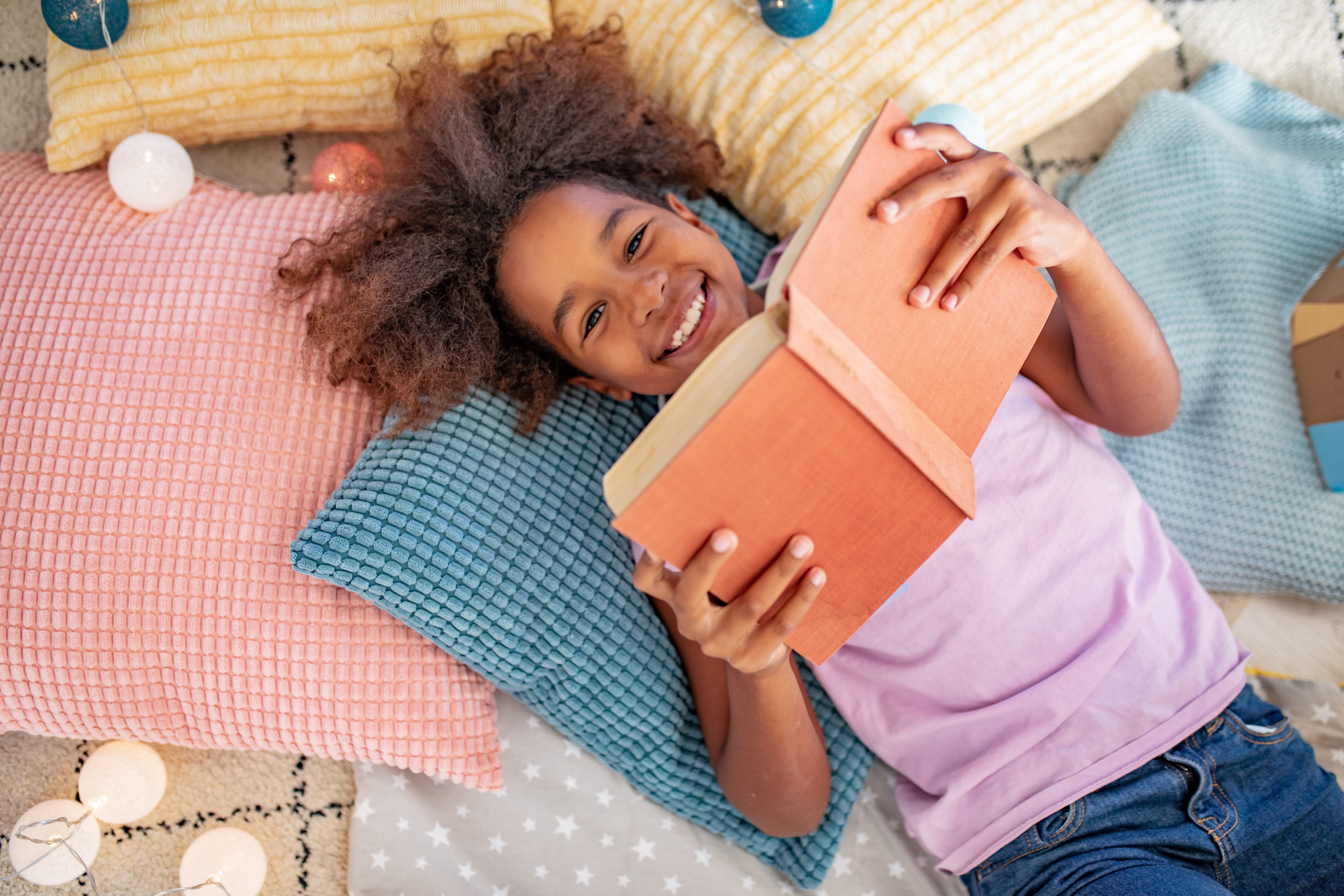 Young Girl Laying on the Pillows and Reading a Book