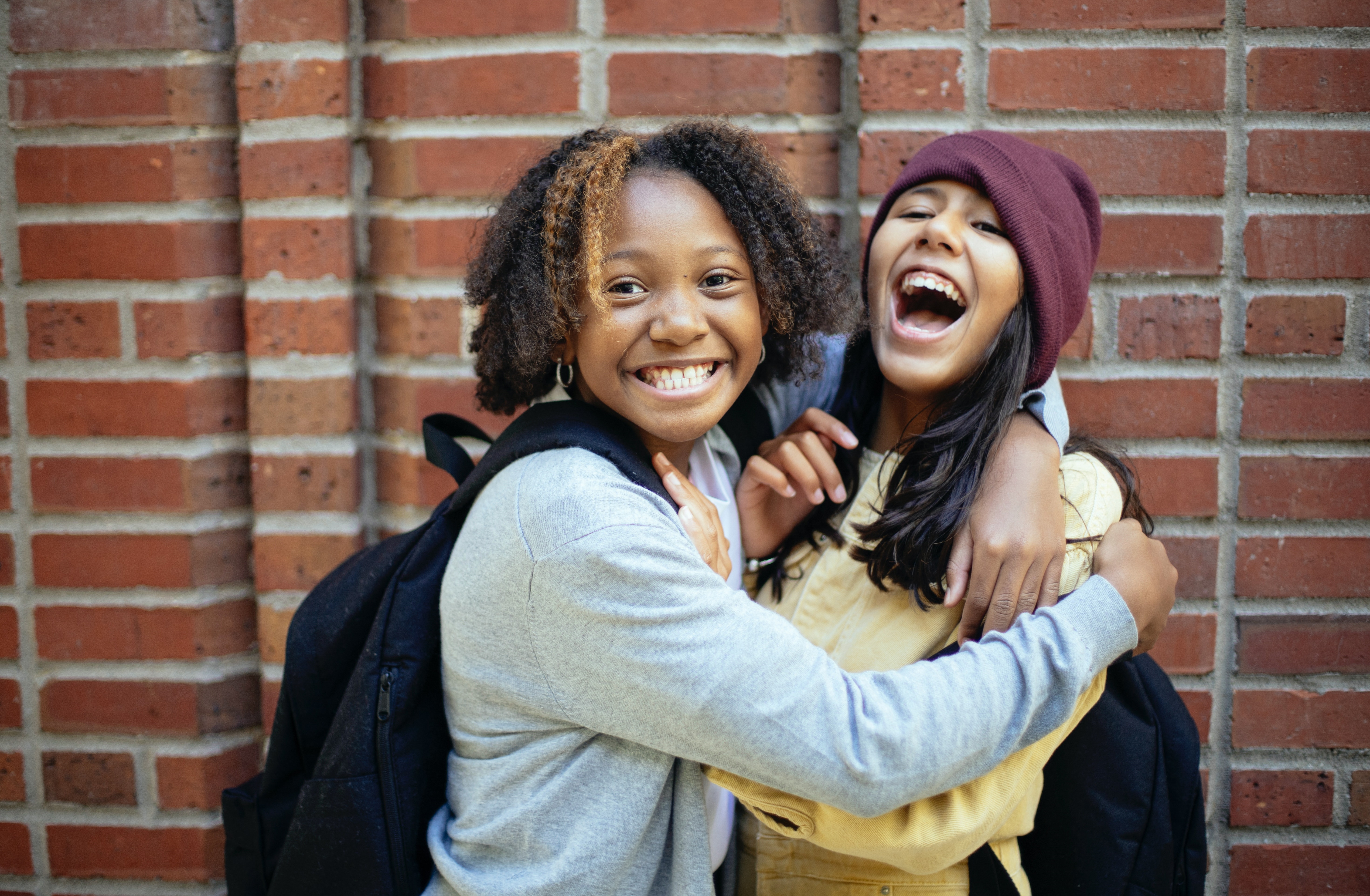 Two Students Embracing near Brick Wall