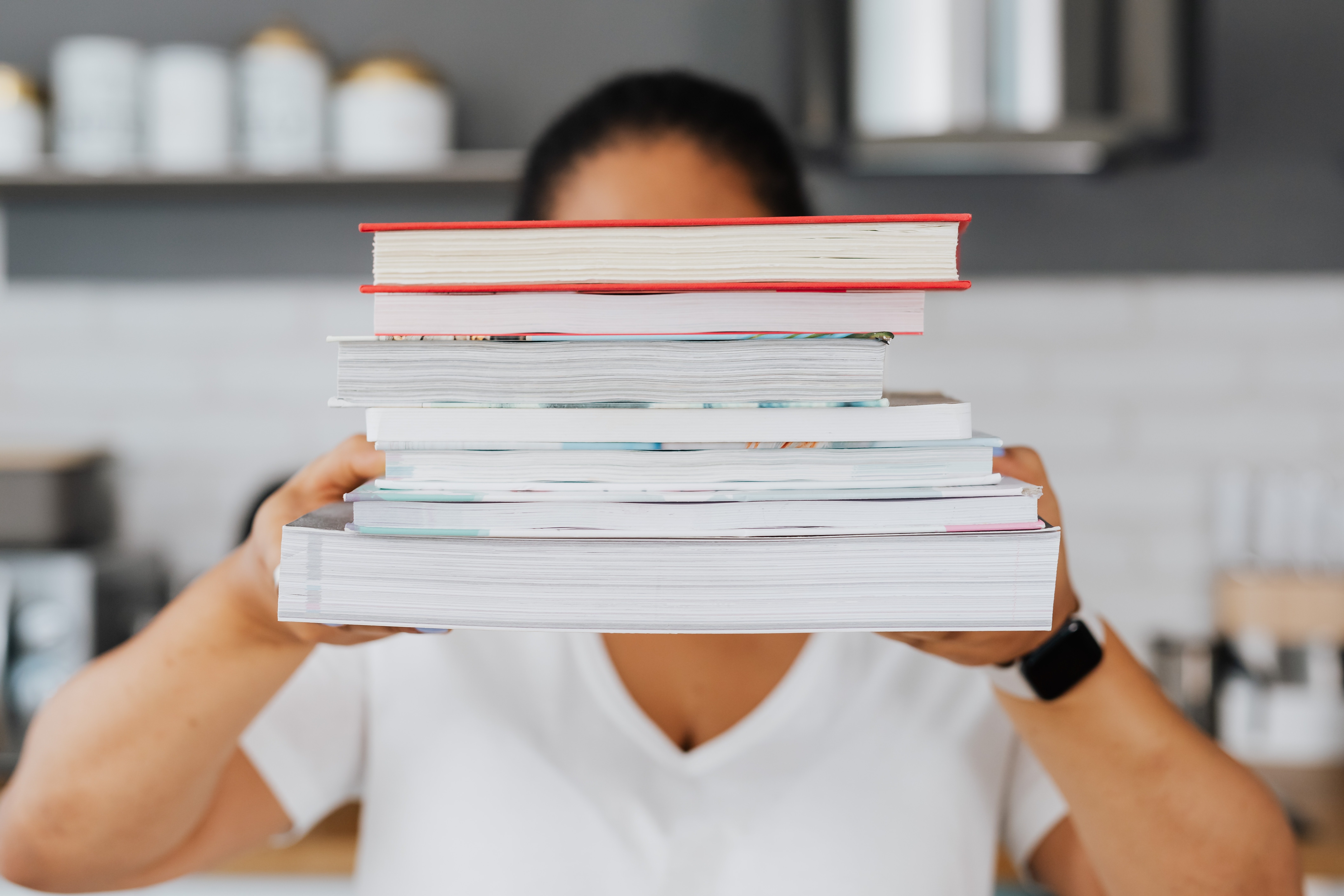 Person Holding a Stack of Books in Front of Face