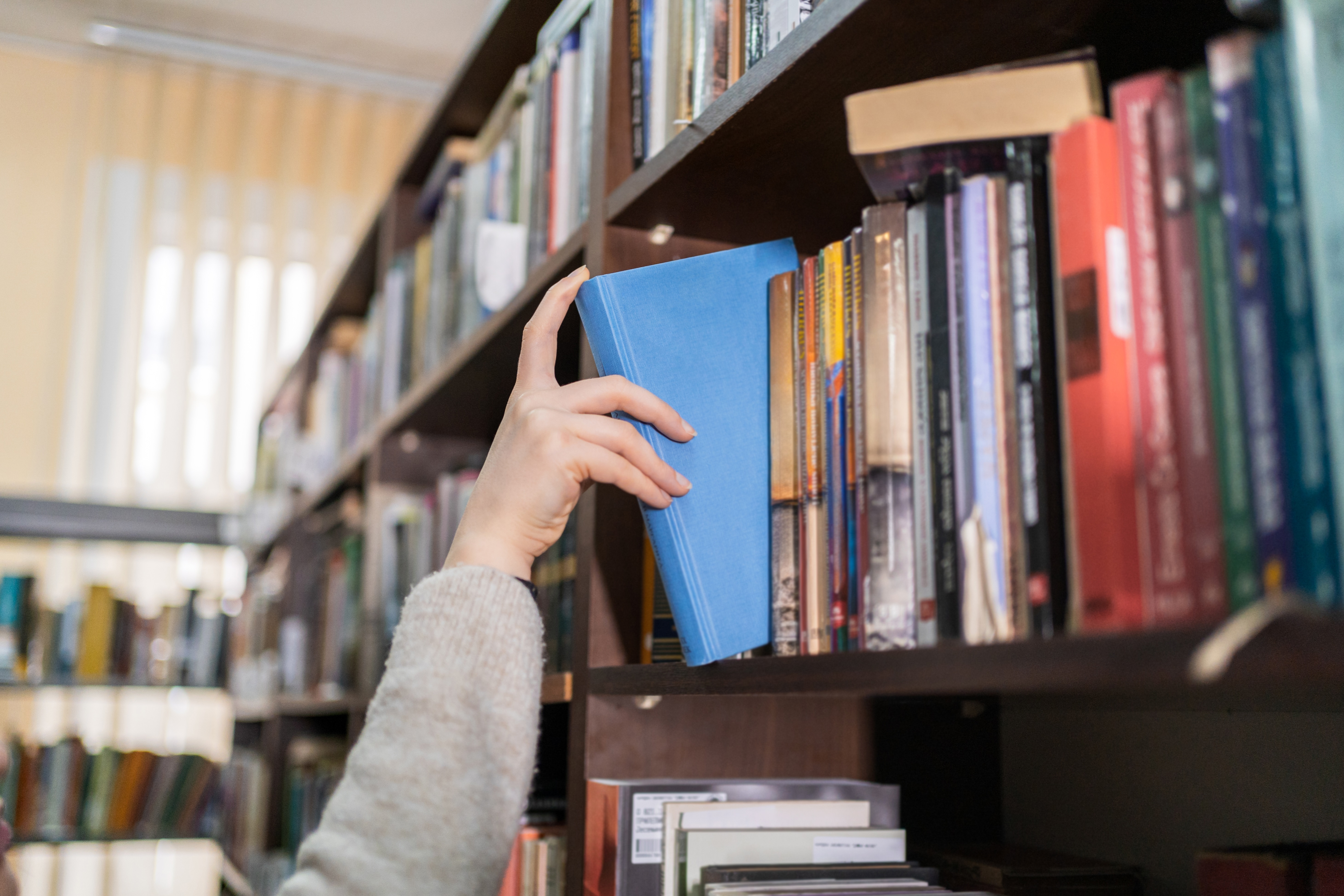 Woman's Hand Picking a Book from a Library Bookshelf