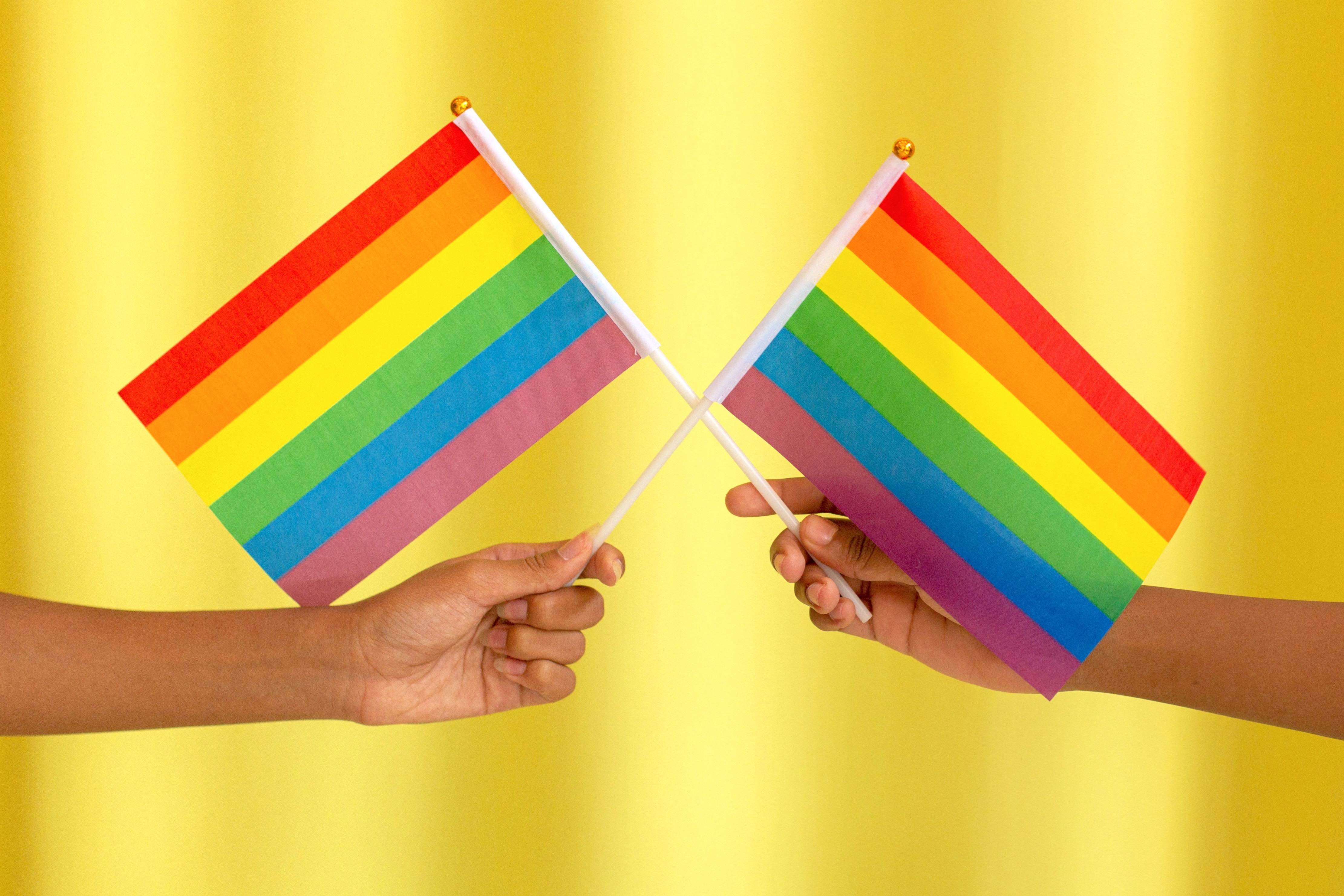 Two People Holding Rainbow Flags Over Yellow Background