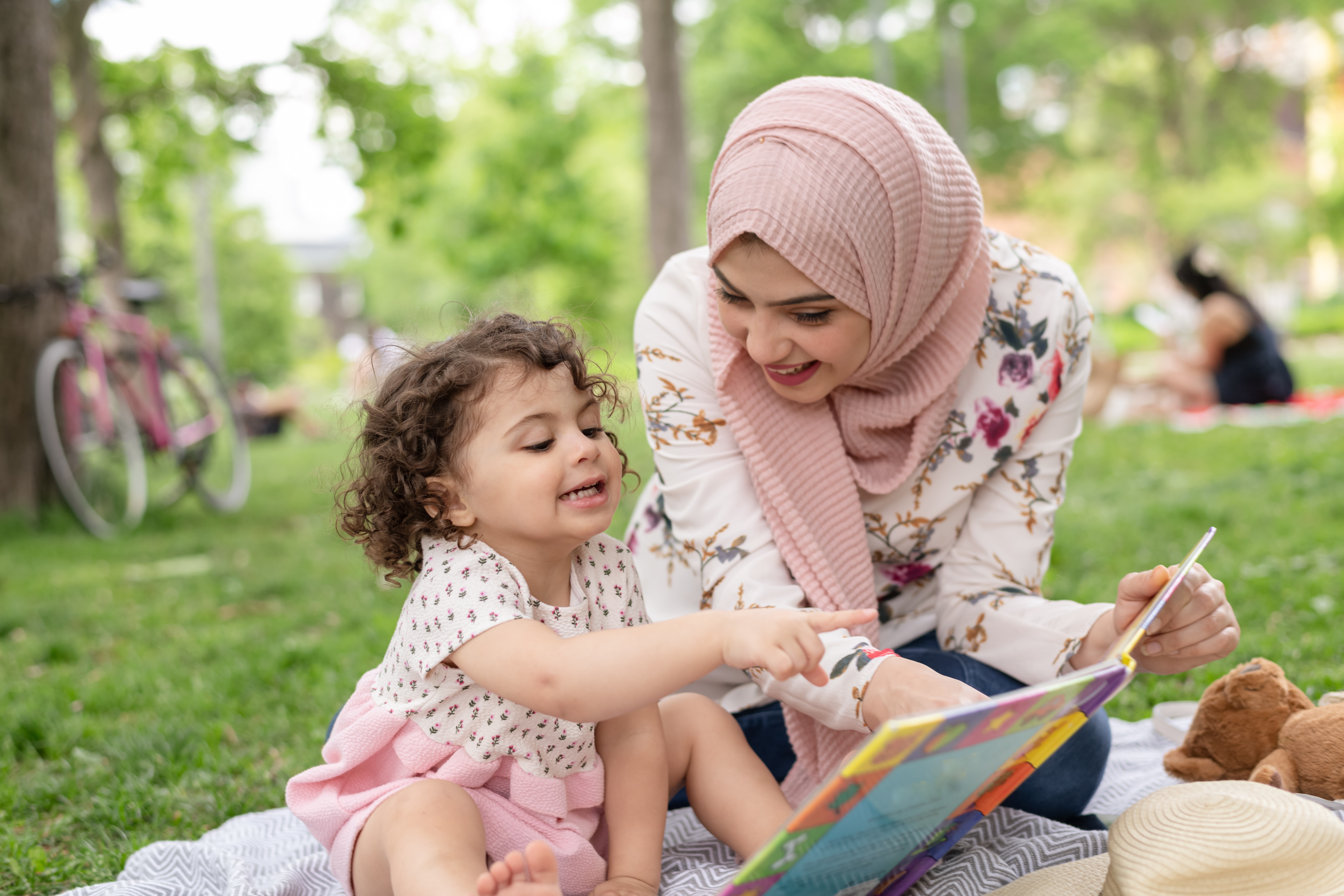 Woman in a Park Reading with Girl on the Grass