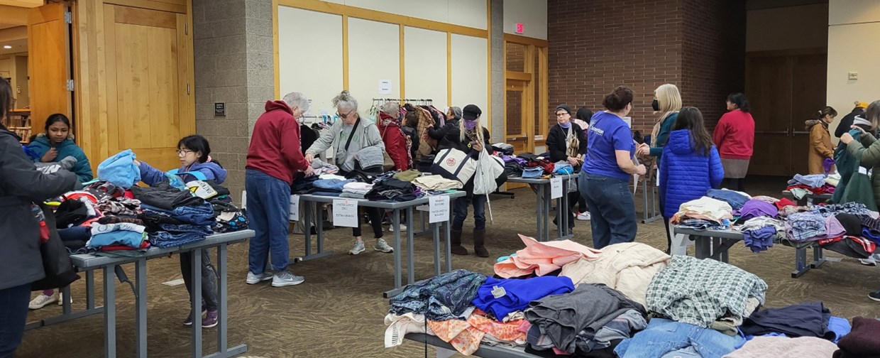 People standing at tables with clothing on top.