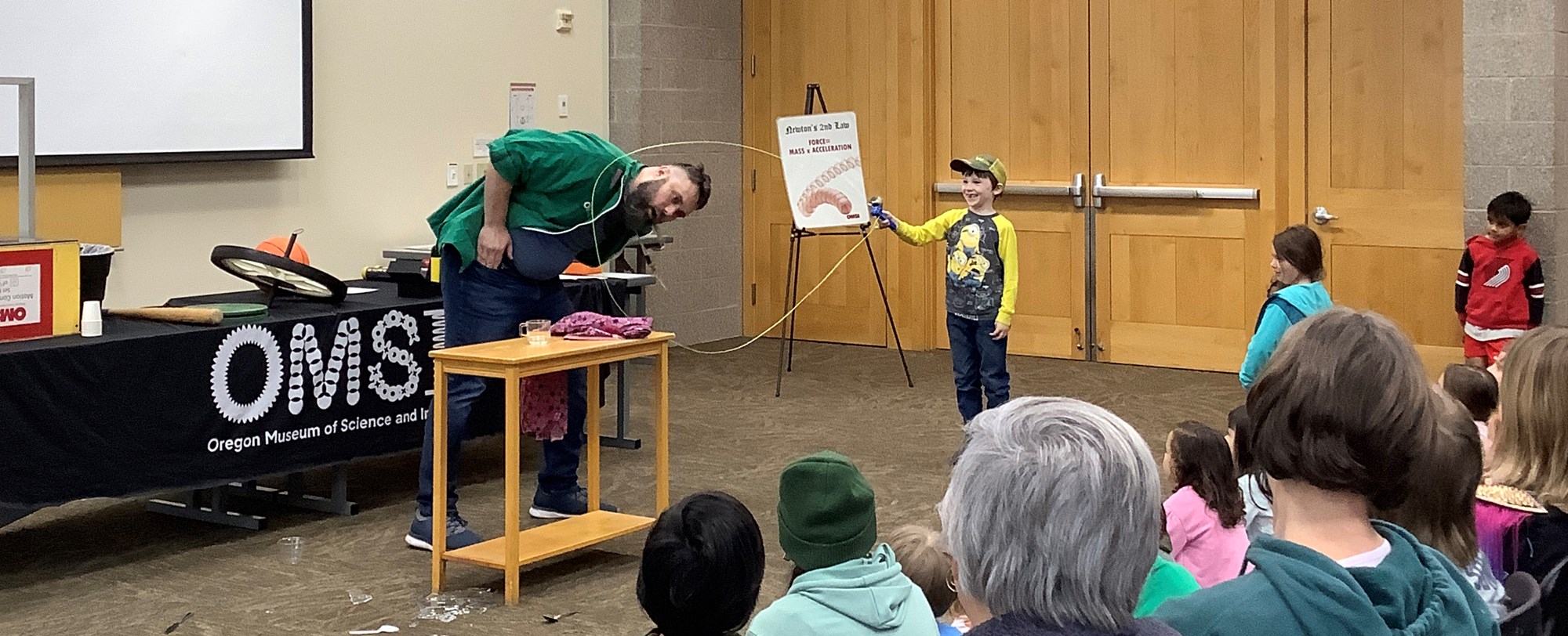 Man with child doing science demonstration in front of crowd.