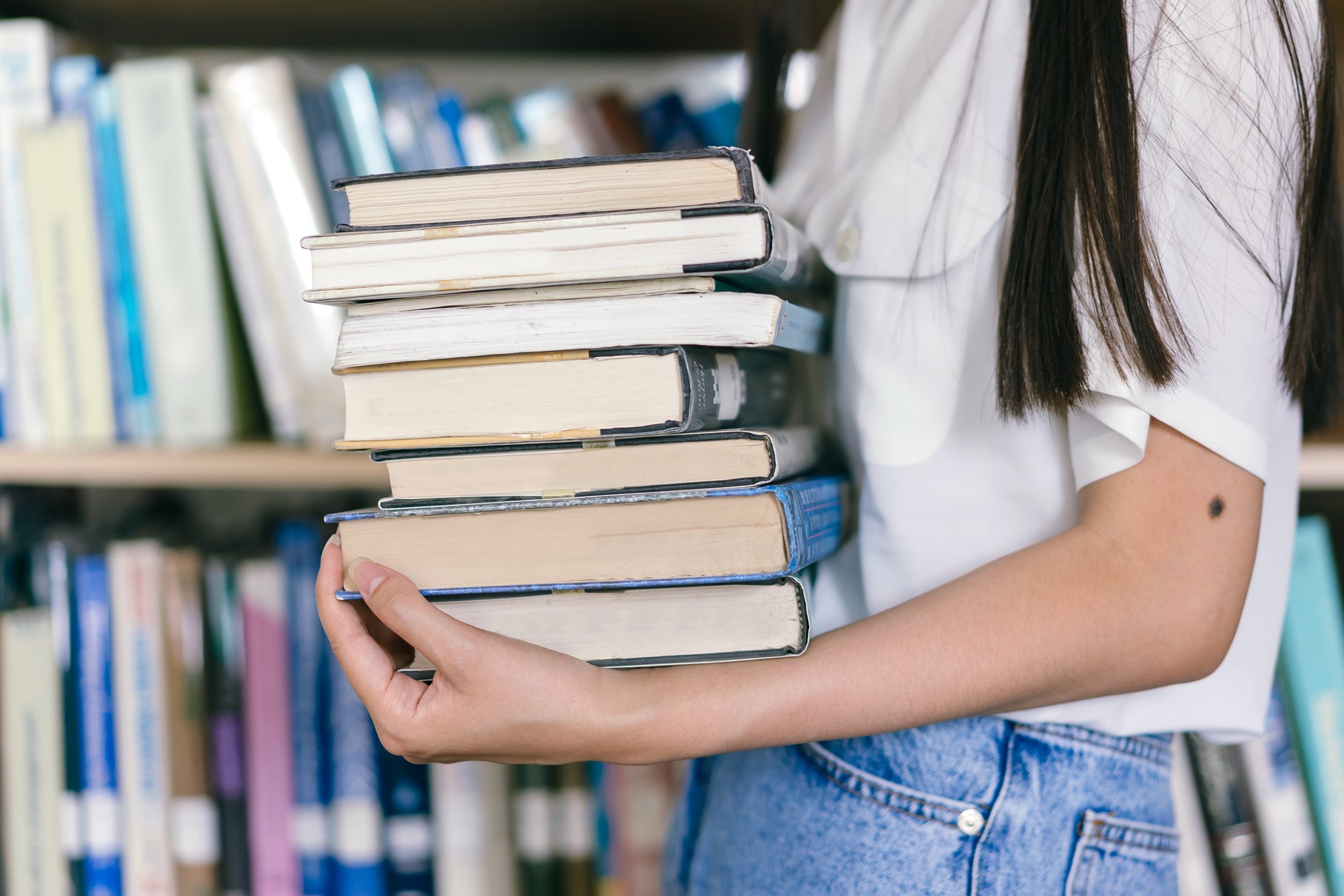 A Person in White Shirt Carrying a Stack of Books