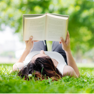 Woman lying in grass reading, Spectacular Summer Reads