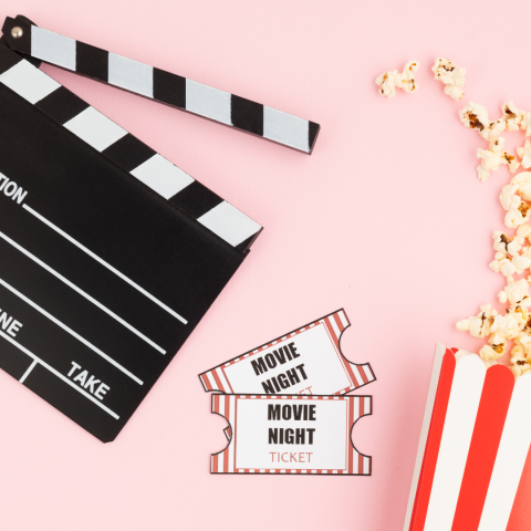 Clapperboard next to 2 tickets next to spilled popcorn