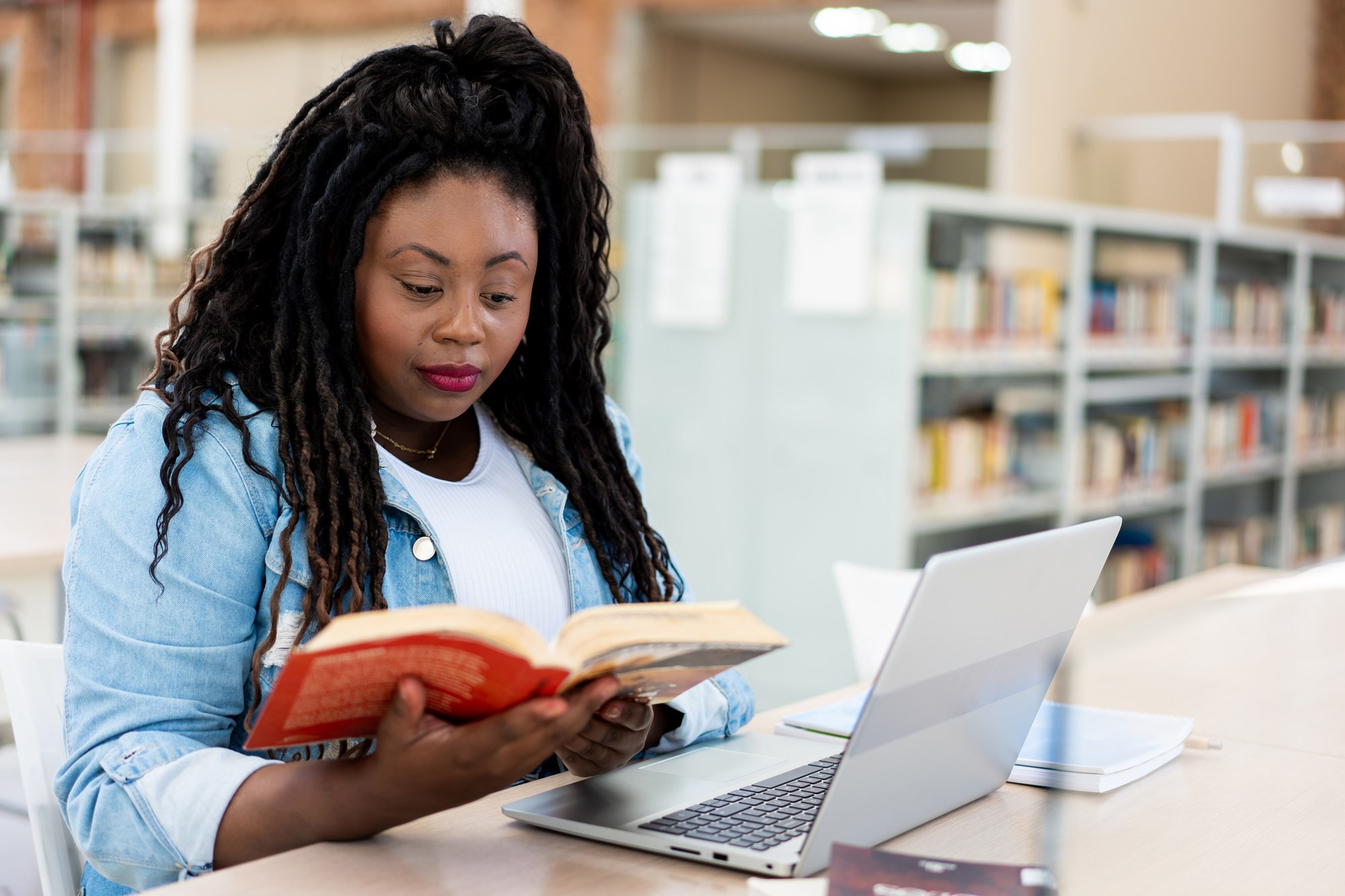 adult woman reading a book in front of her laptop adult woman reading a book in front of her laptop