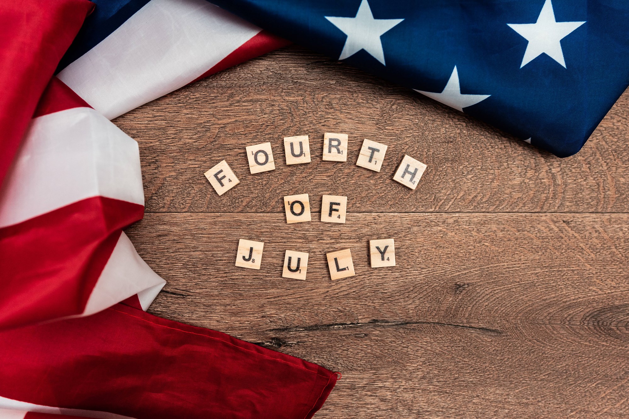 fourth of July written on a table in letter tiles next to an American flag fourth of July written on a table in letter tiles next to an American flag