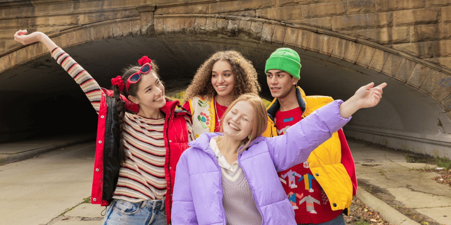 Photo of four late teens in a group. All are smiling and two are holding their hands up in a celebratory way.