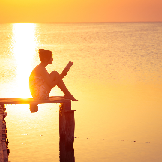 Woman reading on a pier at sunset.