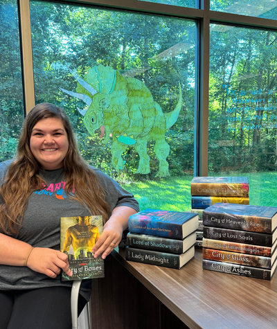 Smiling library worker holding City of Bones and surrounded by the rest of series.