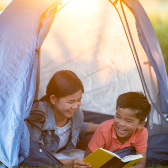 Two children reading in a tent at sunset.