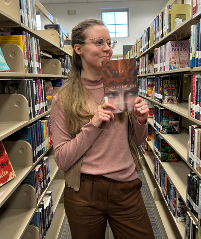 Library employee standing in-between bookshelf holding Poems: Helen of Troy, 1995 by Maria Zoccola