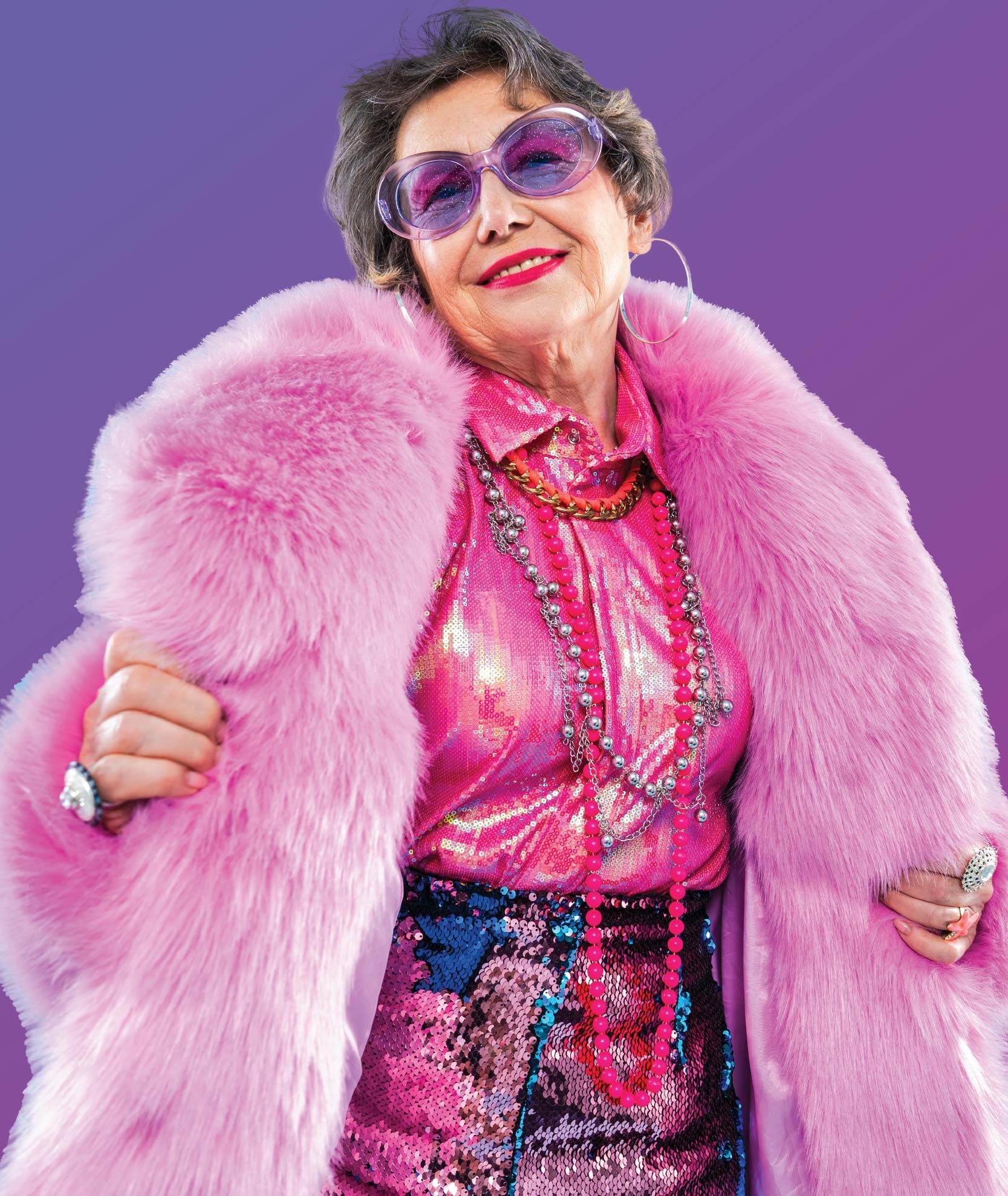 Happy senior lady dressed in pink, from her oversized coat and sunglasses to her metallic shirt.