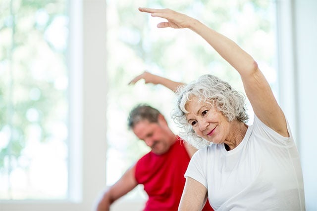 Two older people doing yoga stretches.