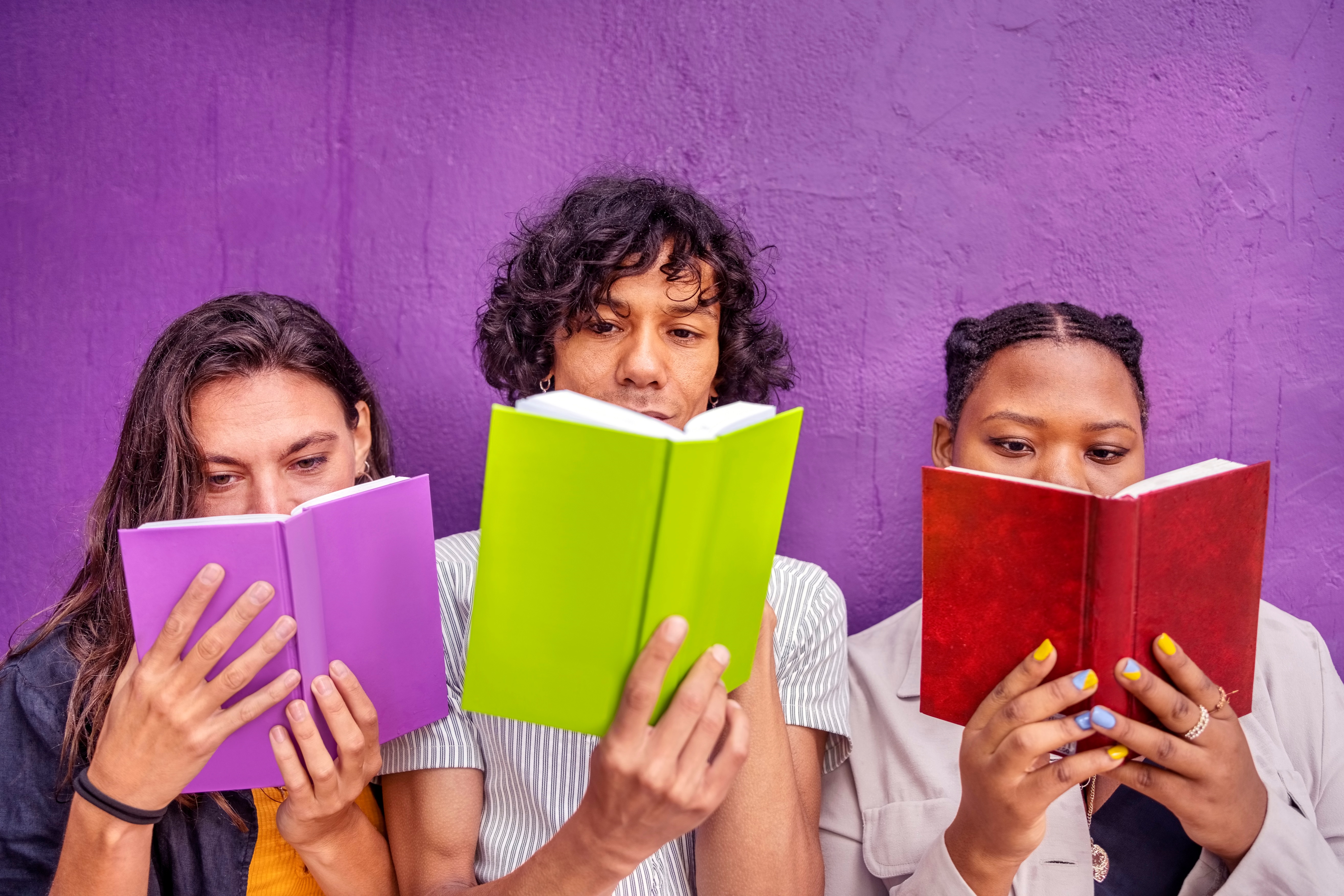 Young Friends Reading Books Against Purple Wall