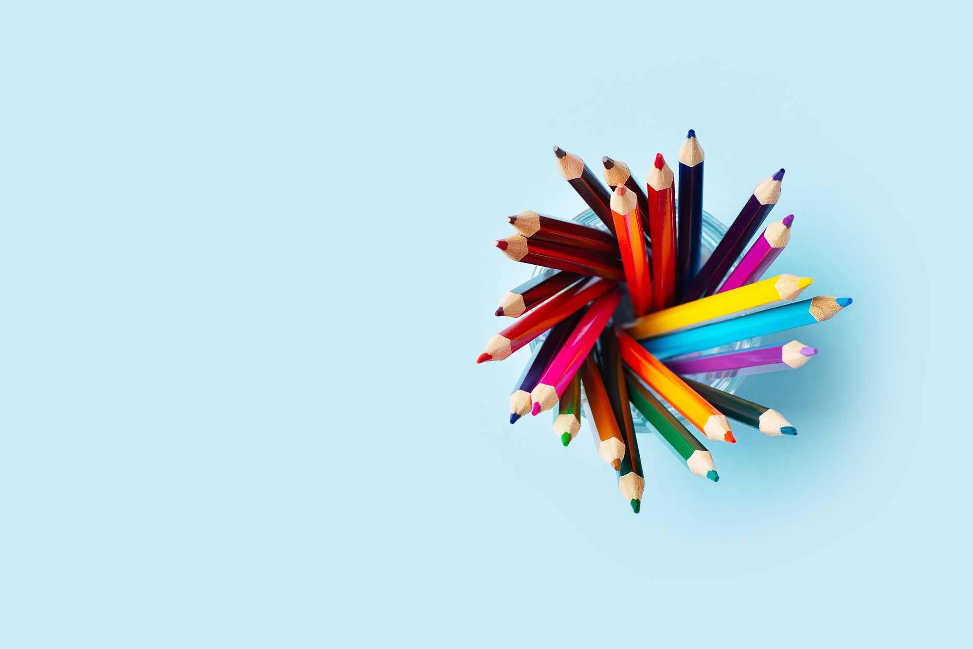 Colored pencils in cup on blue background Colored pencils in cup on blue background