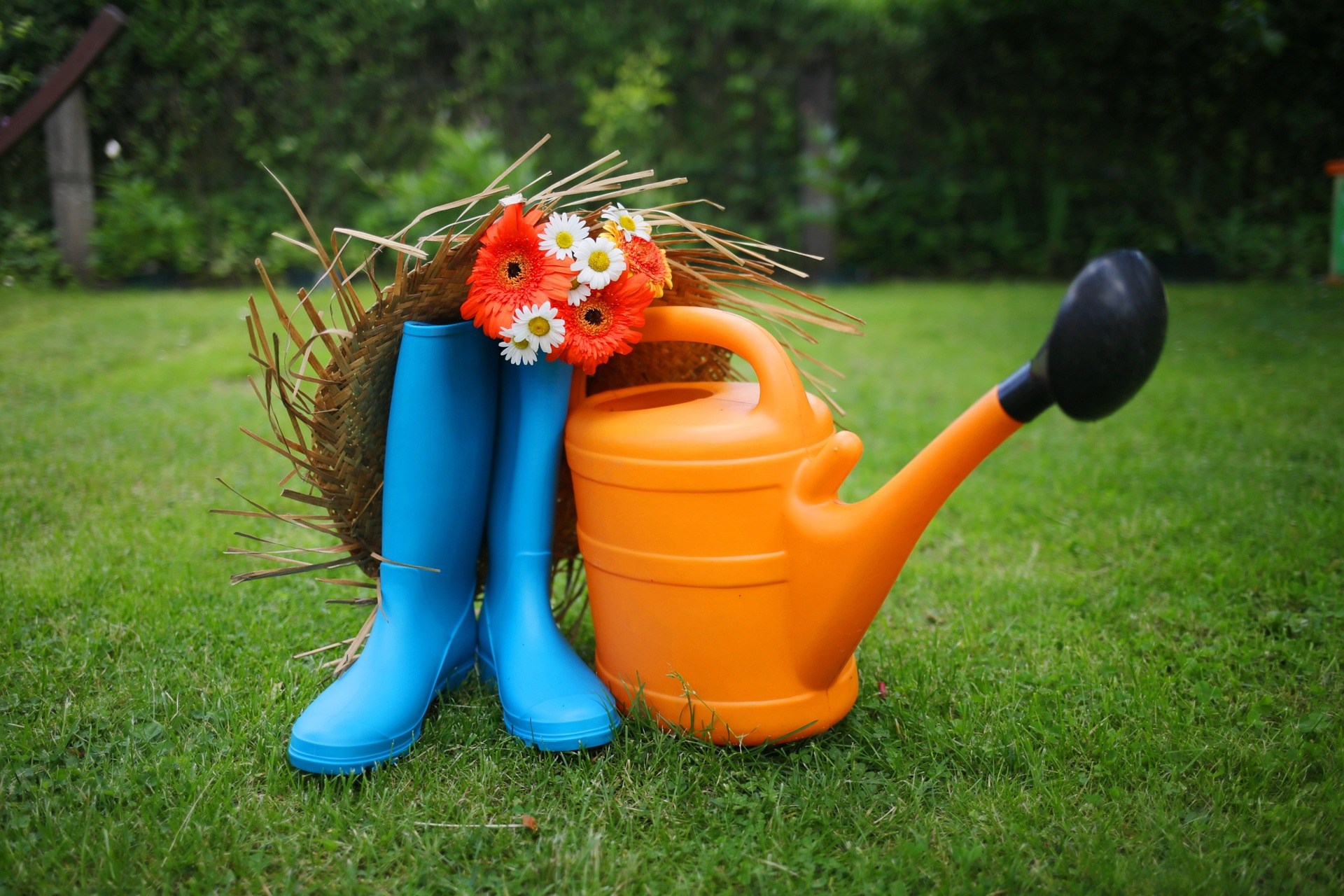Orange watering can next to blue rubber boots on grass
