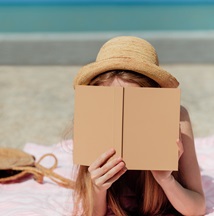 young woman in straw hat reading a book on the beach