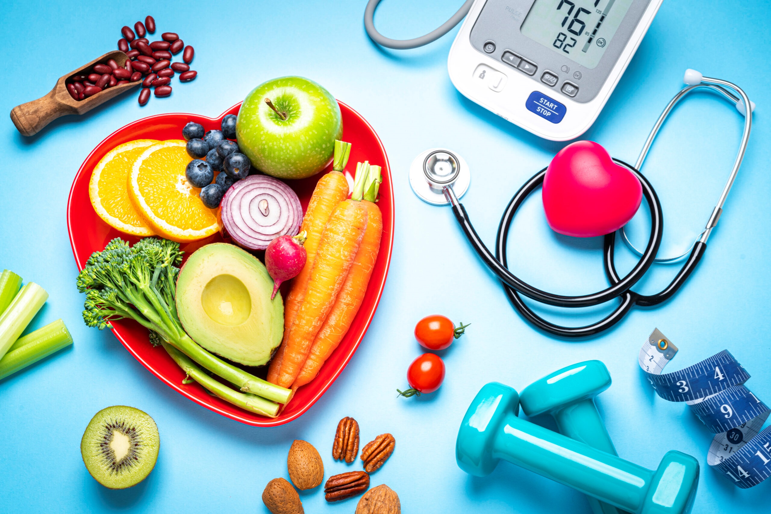 image of heart shaped platter of fruits and vegetables, stethascope, digital health monitor, dumbells, body tape measure, beans, nuts
