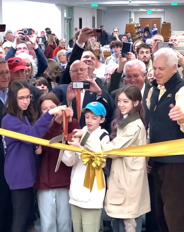 large crowd with 4 children cutting gold ribbon with large pair of scissors