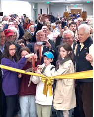 large crowd with 4 children cutting gold ribbon with large pair of scissors